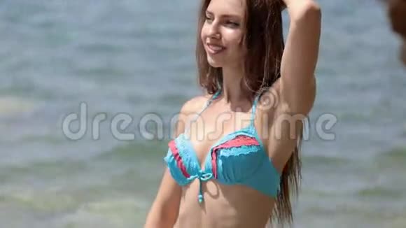 一位留着长发和比基尼的年轻女士站在岩石海滩上摆姿势视频的预览图