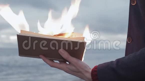 手里拿着燃烧着的书的年轻人站在海岸上背景是风暴云视频的预览图