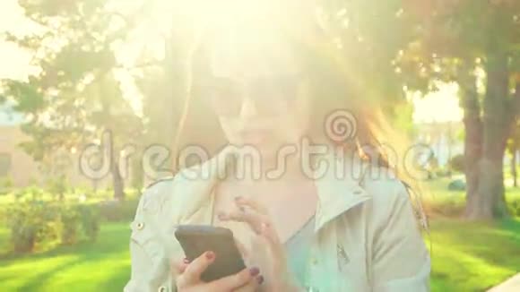 年轻红头发女士户外短信智能手机的肖像女看镜头站在春树旁视频的预览图