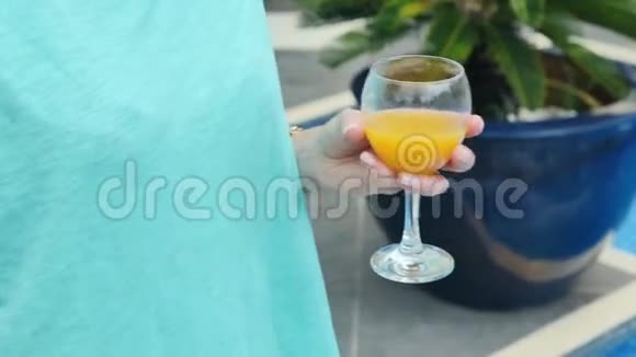 靠近游泳池边握着一杯橙汁的女性手视频的预览图