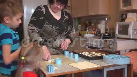 祖母带着孙子和孙女在厨房的桌子上做饼干视频的预览图