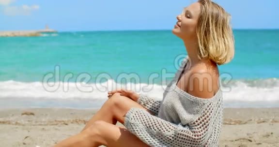 穿灰色毛衣的女人坐在沙滩上视频的预览图