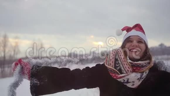 快乐的年轻女子戴着圣诞帽在户外玩得很开心在冬天的雪天里转得很慢视频的预览图