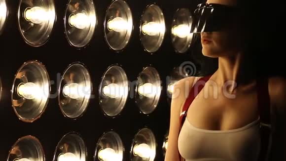 一个穿着内衣的漂亮而奢华的女人在聚光灯的背景下在黑暗的工作室里关闭视频的预览图