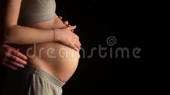 近距离拍摄的孕妇平滑裸露的腹部和未来的父亲轻轻地握住他的妻子的手抚摸视频的预览图