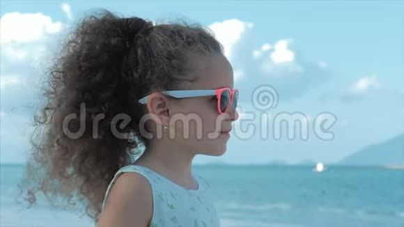 特写肖像一个漂亮的小女孩戴着粉红色的眼镜可爱的微笑着看着大海概念儿童视频的预览图