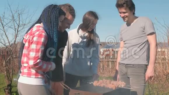 一群年轻人朋友在后院的木炭烤架上烤着沙什利克肉一起聊天和微笑视频的预览图