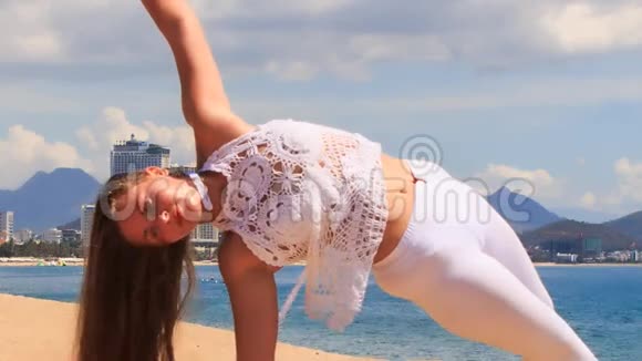 穿花边衣服的金发女孩在海滩上表演瑜伽体式半月视频的预览图