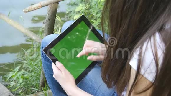 女性手使用数字平板电脑绿色屏幕坐在湖边的木制码头视频的预览图