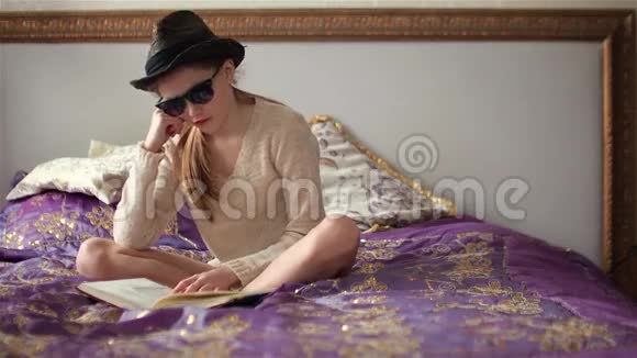 戴太阳镜戴帽子的小女孩坐在床上看书视频的预览图