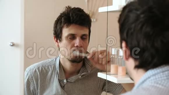疲惫的困倦男人一个宿醉的人刚刚醒来刷牙看着他在镜子里的倒影视频的预览图