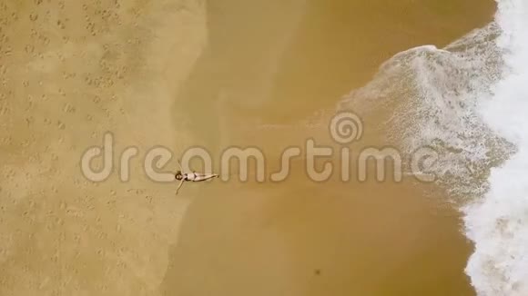 一个穿比基尼的女人躺在沙滩上海浪拍打她的脚视频的预览图