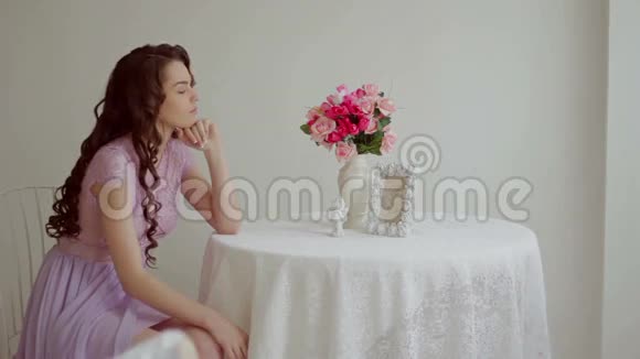 一位身穿粉红色连衣裙的深褐色美女坐在餐桌旁视频的预览图