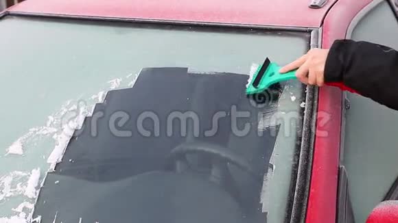 手正从汽车的挡风玻璃上刮冰视频的预览图