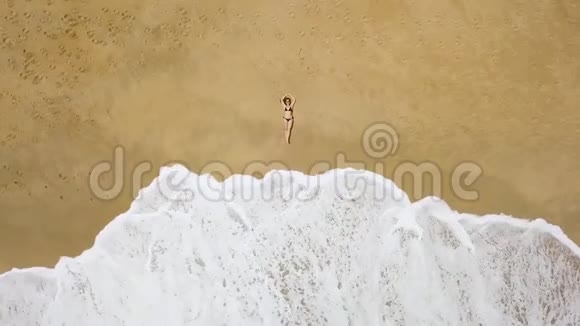 一个穿比基尼的女人躺在沙滩上海浪拍打她的脚视频的预览图