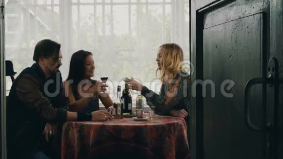 两个女孩和男人在桌子上说话在乡间别墅的露台上喝酒视频的预览图