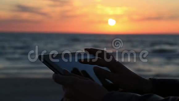 在海边在阳光和背景下在海上和海洋日落时用平板电脑关闭女性的手视频的预览图