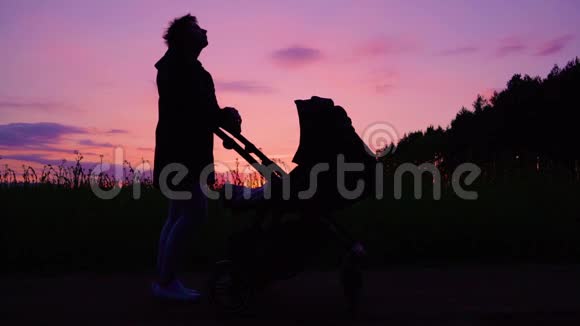 日落时分一位年轻的母亲带着婴儿车在油菜地附近散步视频的预览图