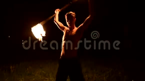 特写镜头低调年轻的男性长着长发赤裸的躯干在黑色的夜晚缓慢地旋转燃烧的火炬视频的预览图