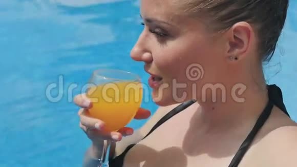 一个微笑的女人在游泳池里喝一杯橙汁的肖像视频的预览图
