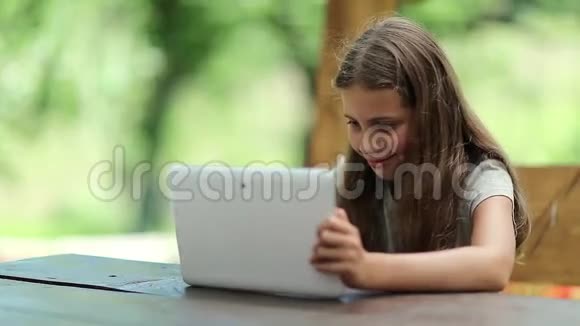 有着平板电脑的漂亮女孩坐在避暑别墅的桌子旁视频的预览图
