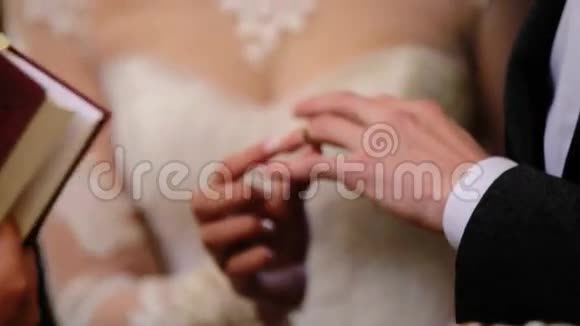 漂亮漂亮的新娘穿着时髦的白色婚纱把金戒指戴在一个穿着黑色的年轻新郎的手指上视频的预览图