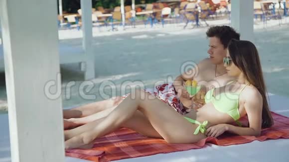 快乐的一对情侣在海滩上休息边说边喝鸡尾酒视频的预览图