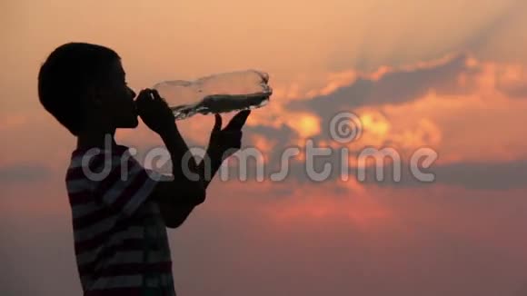 日落时分男孩喝着瓶子里的水剪影茶壶视频的预览图