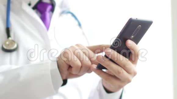 身穿白大褂的男医生用的是带有触摸屏的现代智能手机视频的预览图
