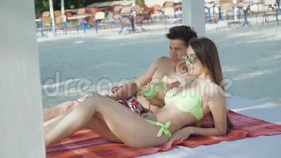 快乐的一对情侣在海滩上休息边说边喝鸡尾酒视频的预览图