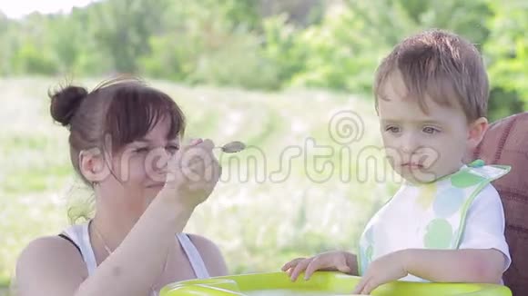 坐在母亲旁边的小男孩用勺子喂孩子的桌子视频的预览图