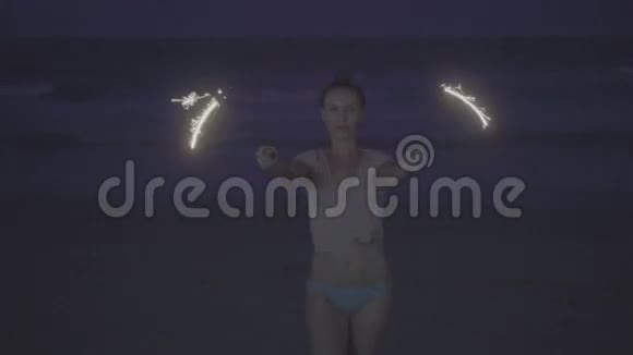 晚上在海滩上用闪闪发光的烟花为幸福的女人做特写视频的预览图