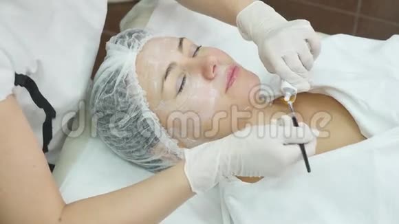 在女性脸上涂奶油面膜的美容师的手她拿着刷子美丽的年轻女子是视频的预览图
