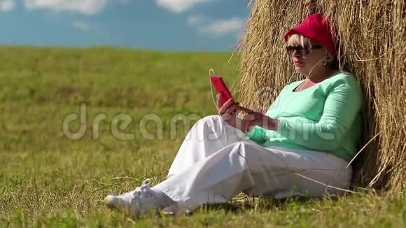 女人坐在干草堆附近的绿草上用手机视频的预览图
