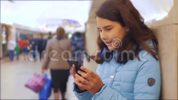 十几岁的女孩带着智能手机和耳机等待地铁很多人挤在地下交叉路口地下地铁视频的预览图