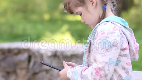 小女孩坐在石墙上玩平板电脑视频的预览图