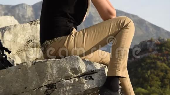 年轻的金发女郎坐在山崖边上与美丽的山峰相映成趣视频的预览图