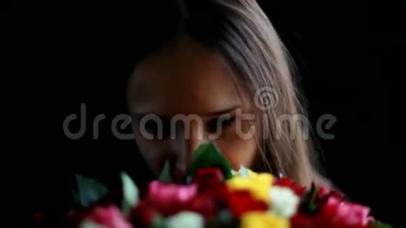一个美丽的女人怀里抱着一大束花闻着一朵芬芳的五颜六色的玫瑰背景是黑色的视频的预览图