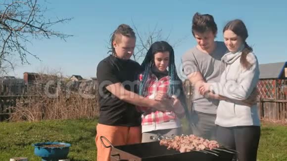 一群年轻人朋友在后院的木炭烤架上烤着沙什利克肉一起聊天和微笑视频的预览图