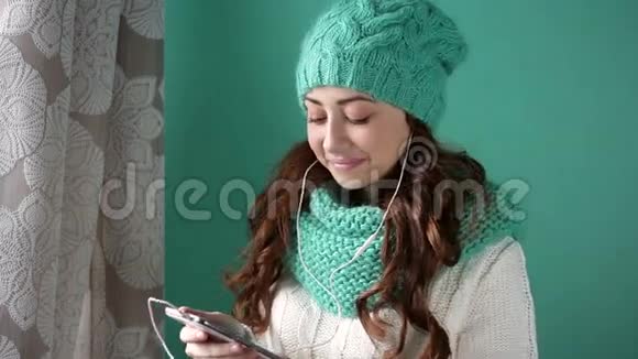 一个漂亮的女孩她拿着手机站在窗边听音乐视频的预览图