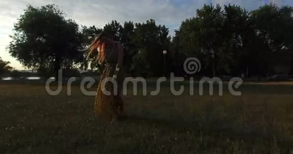 夕阳下美丽的女人光着脚在草地上散步视频的预览图