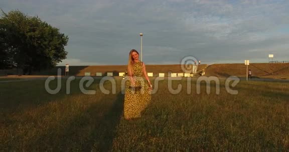 夕阳下美丽的女人光着脚在草地上散步视频的预览图