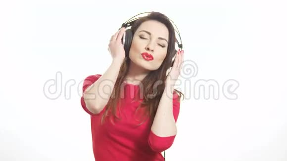 漂亮的红色女孩随着音乐在大耳机中摇摆注意到相机和白色背景上的分离视频的预览图