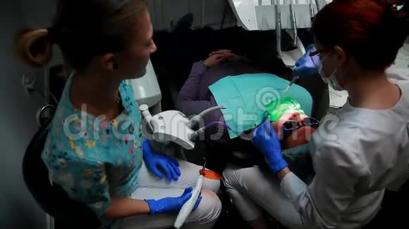 女牙医和她的护士把印章交给躺在牙科办公室椅子上的病人视频的预览图