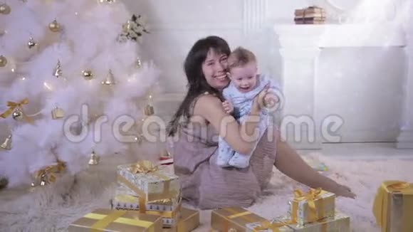 妈妈和宝宝笑着在装饰的新年树旁边玩得很开心树上满是五颜六色的闪闪发光的灯视频的预览图