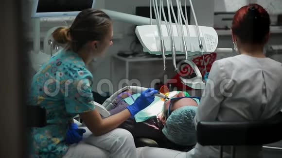 女牙医和她的护士把印章交给躺在牙科办公室椅子上的病人视频的预览图