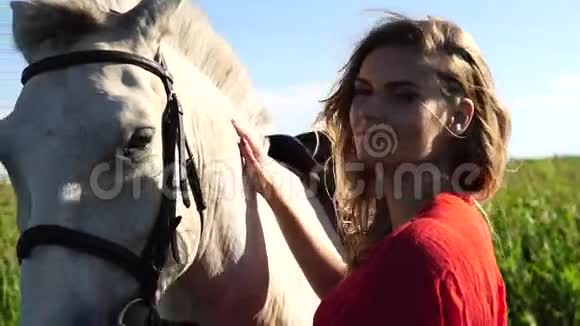 年轻漂亮的女人在田野附近用白色的马着红色的树视频的预览图