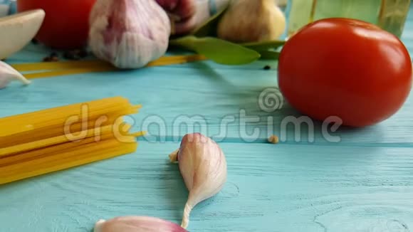 意大利面条油黄传统一瓶素食慢动作大蒜番茄黑胡椒在蓝色木制背景上视频的预览图