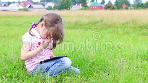小女孩坐在绿色草地上玩平板电脑视频的预览图