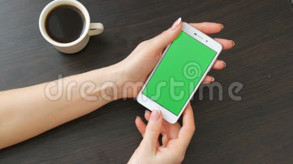 漂亮的法国美甲女性手拿着一个白色智能手机绿色屏幕靠近白色咖啡杯使用视频的预览图